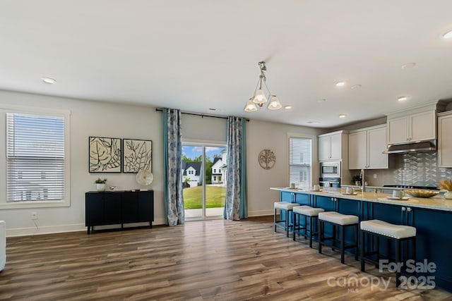 kitchen with a kitchen breakfast bar, stainless steel microwave, baseboards, under cabinet range hood, and dark wood finished floors