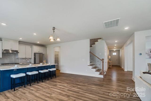 kitchen featuring under cabinet range hood, light wood-style floors, visible vents, and freestanding refrigerator