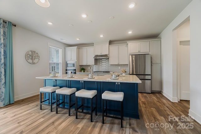 kitchen featuring a center island with sink, appliances with stainless steel finishes, wood finished floors, and baseboards