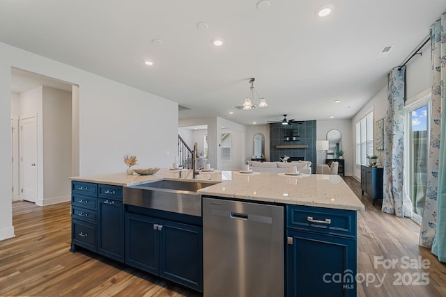 kitchen featuring a sink, light wood-type flooring, blue cabinetry, stainless steel dishwasher, and open floor plan