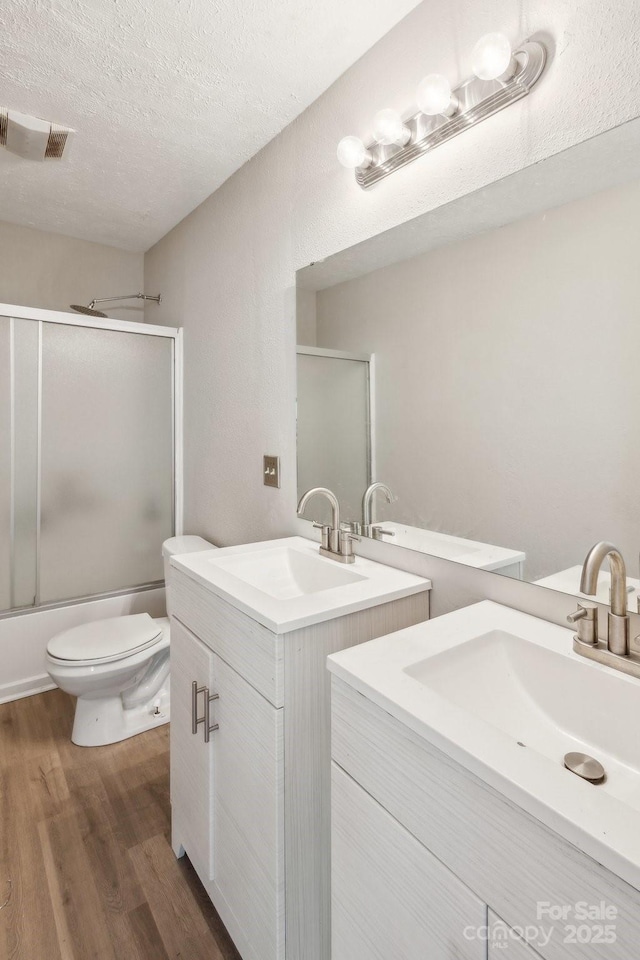 5611 Hammermill Dr, Harrisburg, NC 28075 - full bath featuring two vanities, wood finished floors, a textured ceiling, toilet, and shower / bath combination with glass door