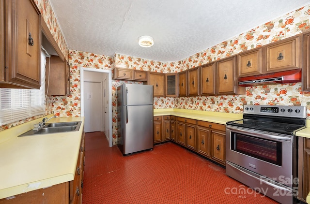 kitchen with stainless steel appliances, wallpapered walls, under cabinet range hood, a sink, and light countertops