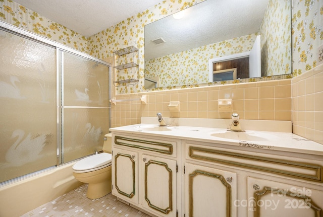 bathroom with wallpapered walls, a textured ceiling, tile walls, toilet, and double vanity