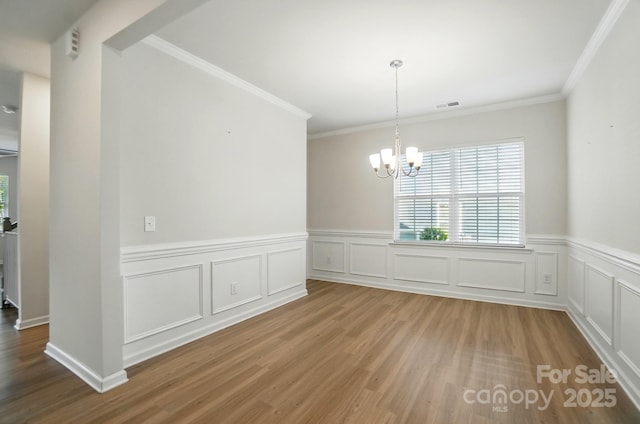 unfurnished dining area with visible vents, a notable chandelier, ornamental molding, wood finished floors, and a wainscoted wall