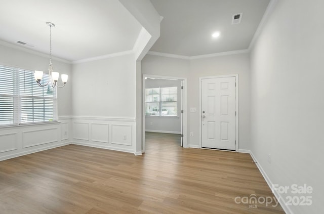unfurnished dining area featuring crown molding, visible vents, light wood-type flooring, and a notable chandelier