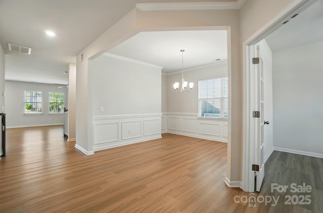 unfurnished dining area featuring ornamental molding, visible vents, a notable chandelier, and wood finished floors