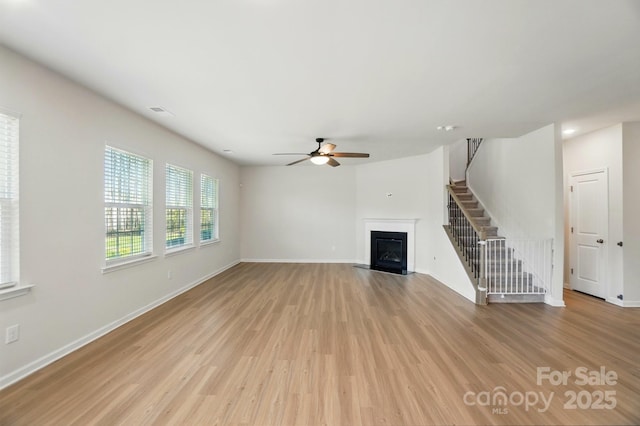 unfurnished living room with stairway, a fireplace with flush hearth, light wood finished floors, and a ceiling fan