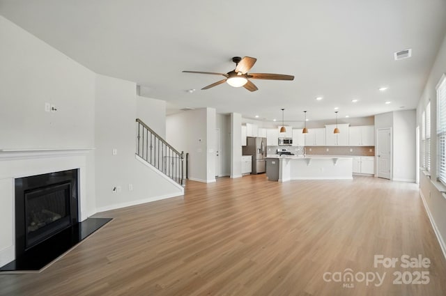 unfurnished living room featuring light wood-style flooring, stairs, a ceiling fan, and recessed lighting