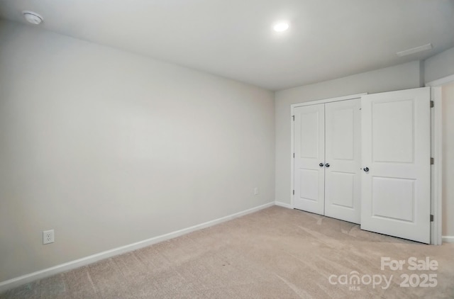 unfurnished bedroom featuring baseboards, a closet, and light colored carpet