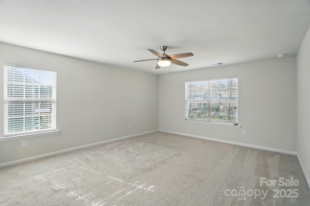 carpeted spare room featuring visible vents, baseboards, a ceiling fan, and plenty of natural light