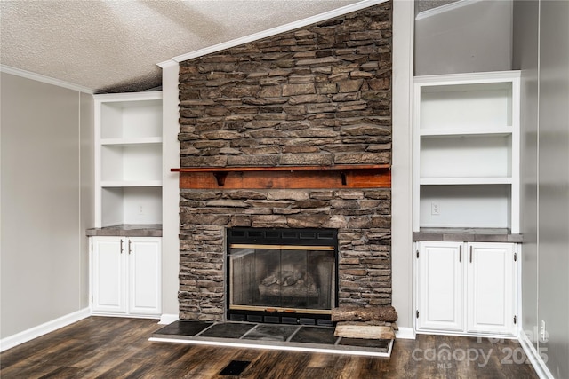 unfurnished living room featuring a textured ceiling, crown molding, dark wood-style flooring, built in features, and a stone fireplace