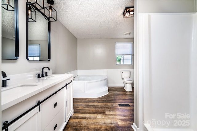 full bath featuring wood finished floors, a garden tub, a wainscoted wall, a sink, and a textured ceiling