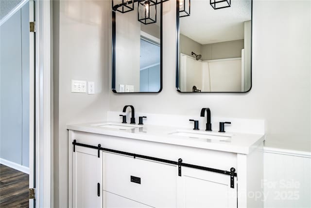 full bath featuring double vanity, wood finished floors, a wainscoted wall, and a sink