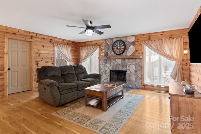 3670 Maple Creek Rd, Rutherfordton, NC 28139 - living area featuring a ceiling fan, light wood-style flooring, a stone fireplace, and wood walls