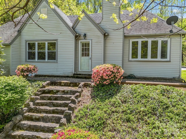 rear view of house with entry steps, a shingled roof, and a chimney