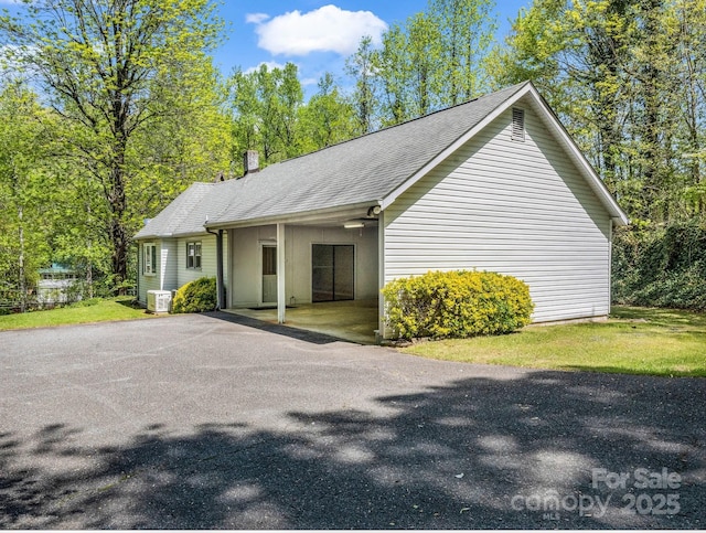view of home's exterior with a chimney, aphalt driveway, a carport, and a shingled roof