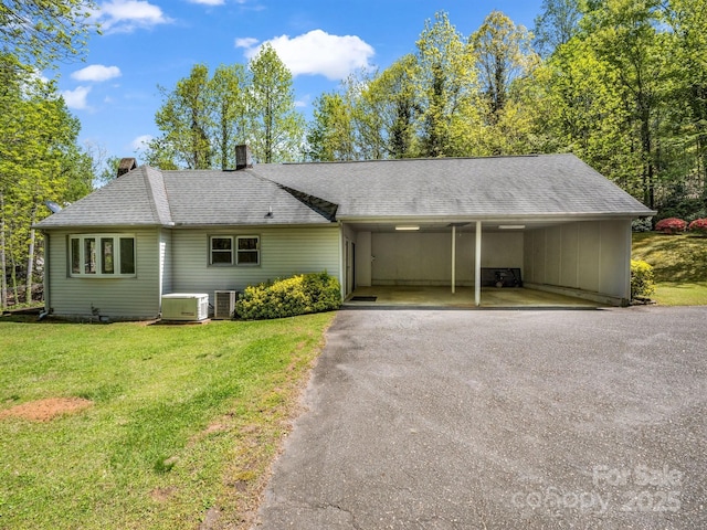 single story home featuring aphalt driveway, a shingled roof, an attached carport, cooling unit, and a front yard