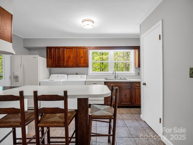 kitchen featuring light countertops, ornamental molding, a sink, washing machine and clothes dryer, and white fridge with ice dispenser