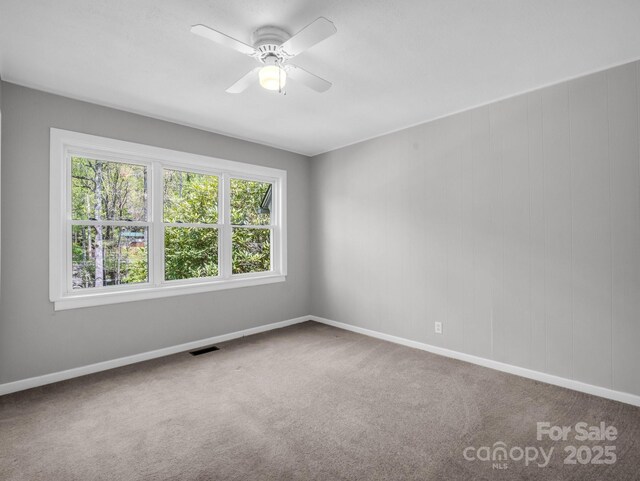 carpeted empty room with baseboards, a ceiling fan, and visible vents