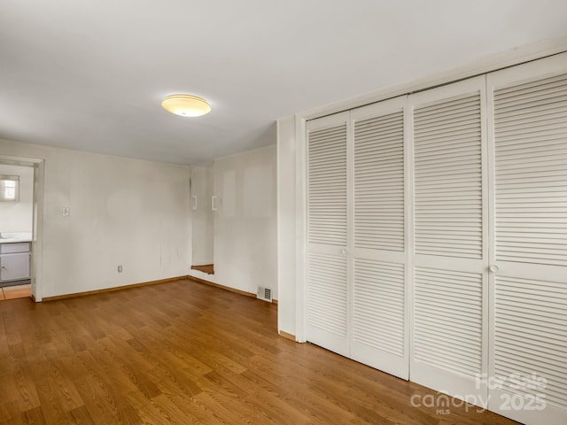 unfurnished bedroom with wood finished floors, a closet, baseboards, and visible vents