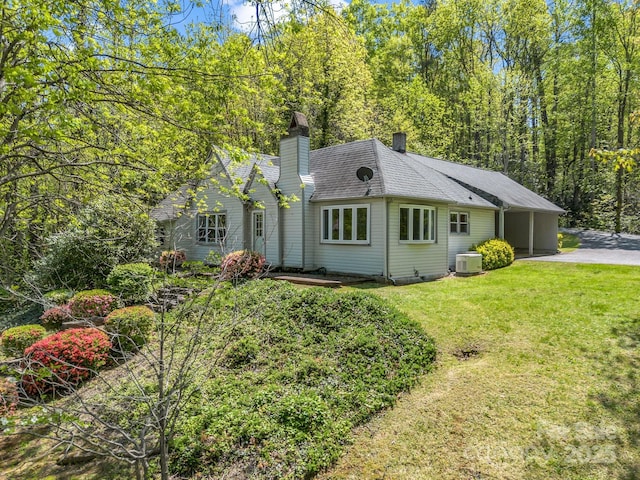 exterior space with a chimney, a yard, central air condition unit, driveway, and an attached carport