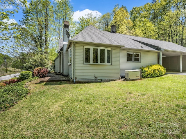 rear view of property featuring a lawn, a chimney, an attached carport, and roof with shingles