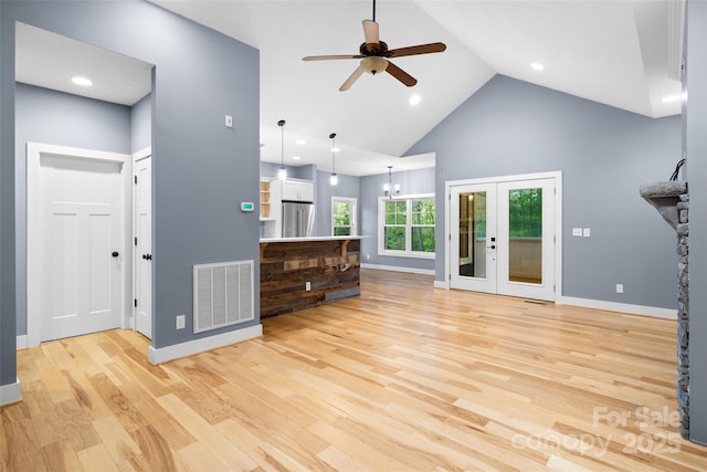 unfurnished living room featuring high vaulted ceiling, light wood-style flooring, ceiling fan with notable chandelier, baseboards, and visible vents