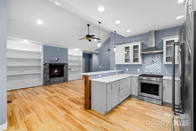 kitchen with a peninsula, wall chimney range hood, a ceiling fan, appliances with stainless steel finishes, and vaulted ceiling