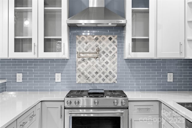 kitchen featuring glass insert cabinets, light countertops, wall chimney exhaust hood, white cabinetry, and gas stove