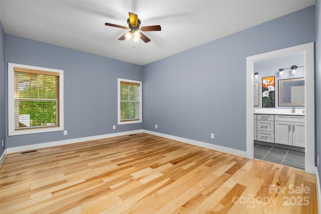 unfurnished bedroom with visible vents, wood finished floors, a sink, baseboards, and connected bathroom