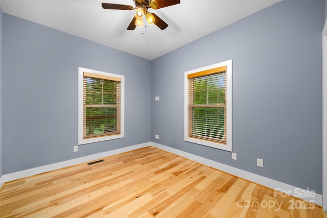 empty room with baseboards, visible vents, a wealth of natural light, and wood finished floors
