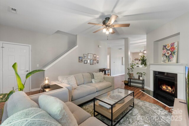 8917 Chalkstone Rd, Charlotte, NC 28216 - living room with a warm lit fireplace, wood finished floors, visible vents, a ceiling fan, and stairs