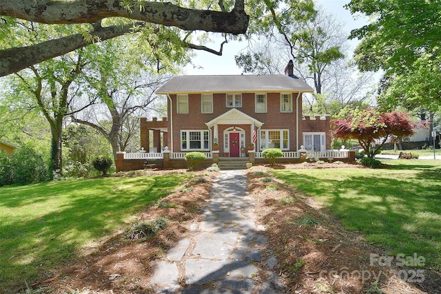 view of front facade featuring a chimney, brick siding, a front yard, and a porch