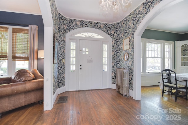 foyer entrance featuring a chandelier, wallpapered walls, wood finished floors, arched walkways, and baseboards