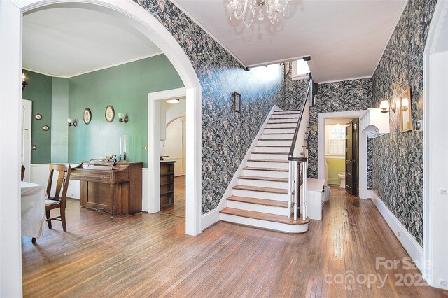 stairway featuring wallpapered walls, ornamental molding, wood finished floors, baseboards, and arched walkways