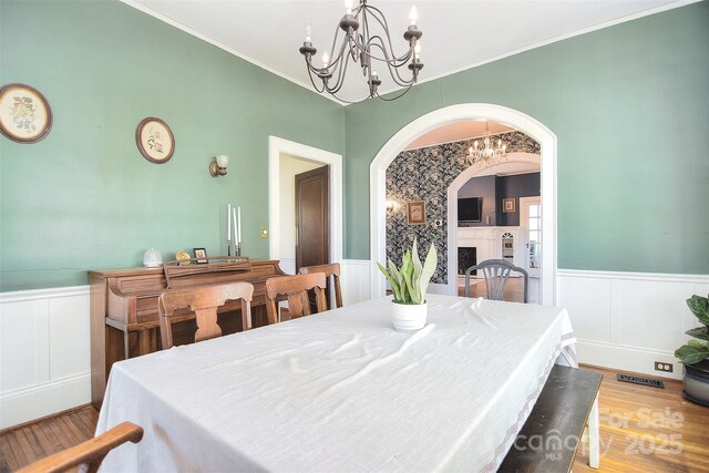dining area with a chandelier, arched walkways, a wainscoted wall, wood finished floors, and a decorative wall