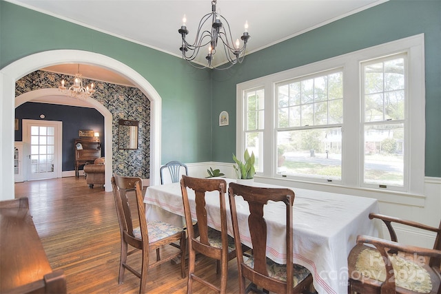 dining space with a chandelier, arched walkways, wood finished floors, a wainscoted wall, and ornamental molding