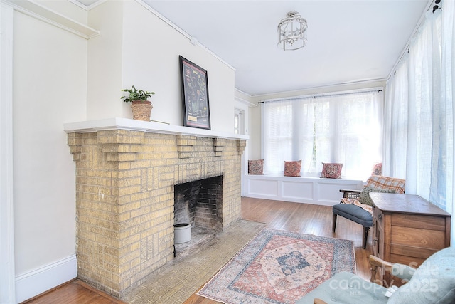 living area with wood finished floors, a brick fireplace, and crown molding