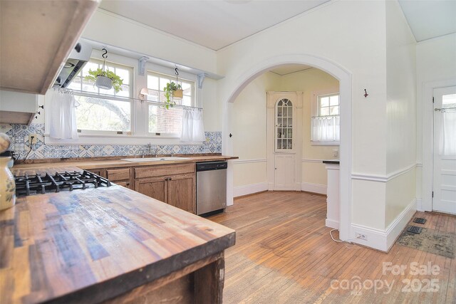 kitchen featuring butcher block countertops, a sink, stainless steel dishwasher, arched walkways, and light wood-type flooring