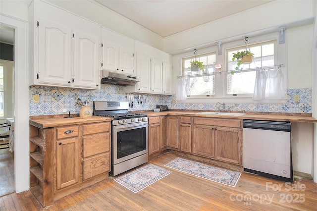 kitchen with stainless steel gas range, dishwashing machine, a sink, butcher block countertops, and under cabinet range hood