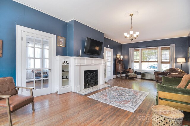 living area with radiator, a chandelier, wood finished floors, a fireplace with flush hearth, and crown molding