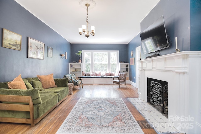 living room with a chandelier, wood finished floors, a fireplace with flush hearth, and ornamental molding