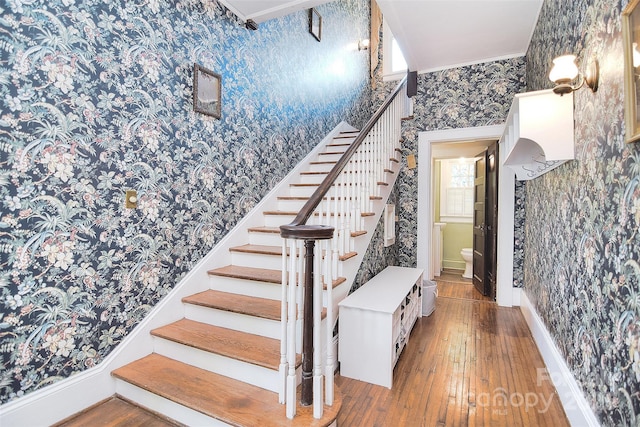 stairs with wallpapered walls, hardwood / wood-style floors, baseboards, and crown molding