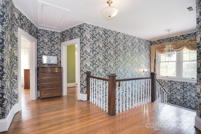 corridor with wallpapered walls, attic access, an upstairs landing, ornamental molding, and hardwood / wood-style floors