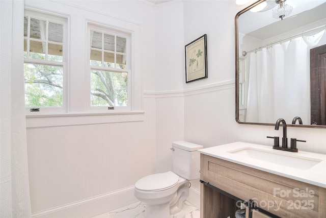 full bath with marble finish flooring, toilet, a wainscoted wall, vanity, and crown molding