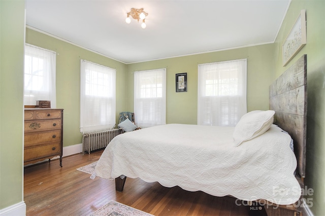 bedroom with radiator, crown molding, wood finished floors, and baseboards