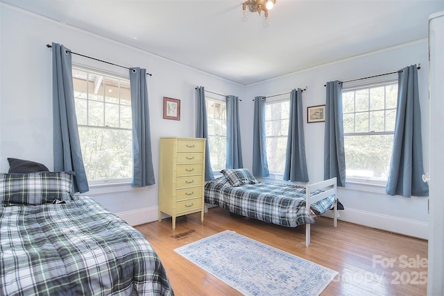 bedroom with multiple windows, wood finished floors, baseboards, and crown molding