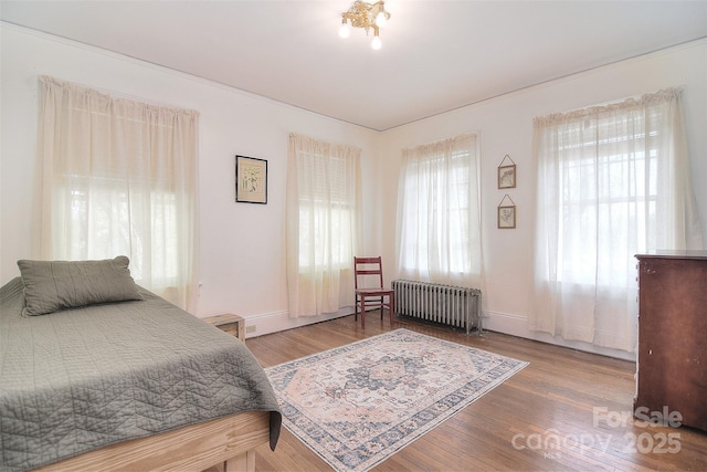bedroom with radiator heating unit, wood finished floors, and baseboards