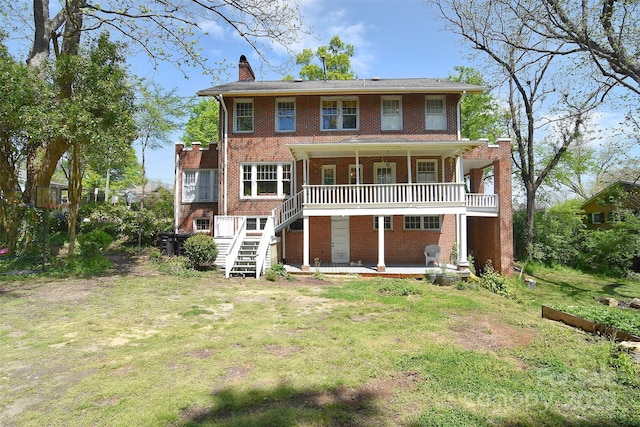 back of house with brick siding, a chimney, covered porch, a lawn, and stairway