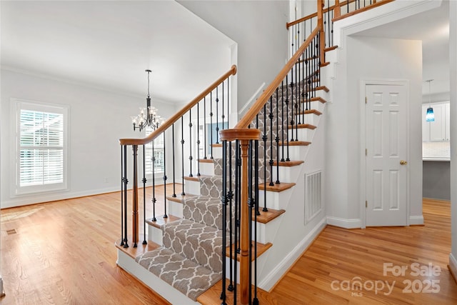 stairway featuring baseboards, a chandelier, wood finished floors, and visible vents